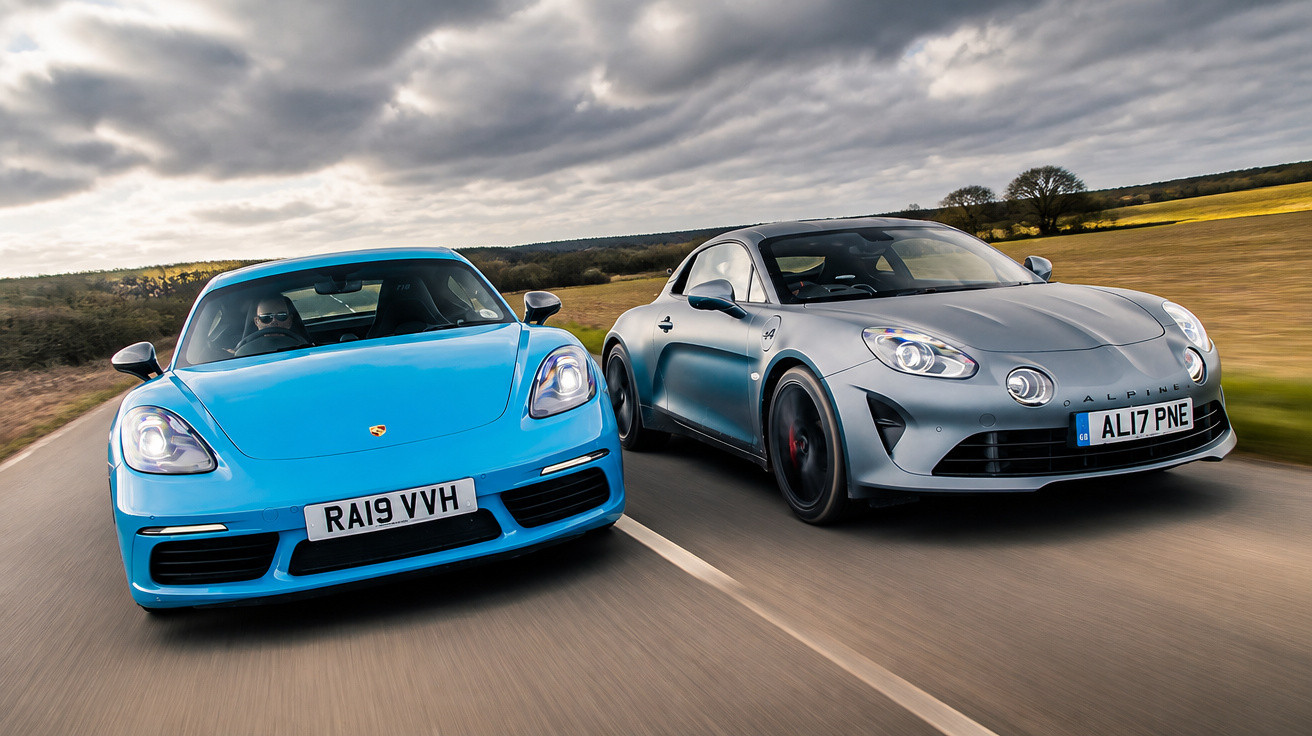 Deux voitures sportives, une Porsche bleue et une Alpine grise, roulant côte à côte sur une route de campagne.